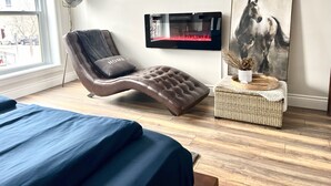 A modern bedroom with a leather recliner, a mounted TV, a horse painting, and a wicker side table.