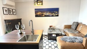 A modern living room with a kitchen area, a sofa, a coffee table, and a cityscape painting on the wall.