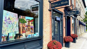 A storefront with a sign reading "Décor à la Mode" and "Voilà!" with a display of colorful paintings and potted red flowers.