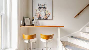 En modern inredning med en trappa, två barstolar, ett inramat konstverk som föreställer en katt och en liten bardisk med glas och en meny.