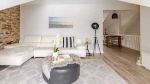 A modern living room with a white sectional sofa, a round ottoman with a fur throw, and a small table with a vase of flowers. There is a painting on the wall and a floor lamp in the corner. - Designer Maisonnette with Stunning Tay Basin and Fountain View (Perth)