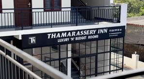 Une enseigne d’hôtel portant le nom « Thamarassery Inn » et la mention « Chambres de luxe et chambres économiques », indiquant le type d’hébergement proposé.