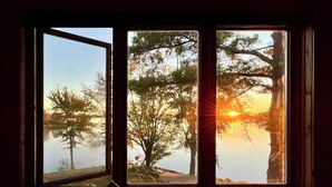 Una stanza con una grande finestra vista su un lago e alberi, con un tavolino e un cannone giocattolo.