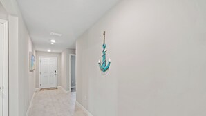 A hallway with a white door at the end, a light-colored tiled floor, and a turquoise anchor decoration on the wall. - Entire New House with Office Space-WiFi, Near JetBlue Park & RSW Airport! (Lehigh Acres)