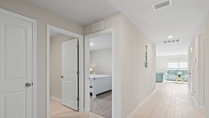A hallway with a bed in the background, a door on the left, and a light-colored floor. - Entire New House with Office Space-WiFi, Near JetBlue Park & RSW Airport! (Lehigh Acres)