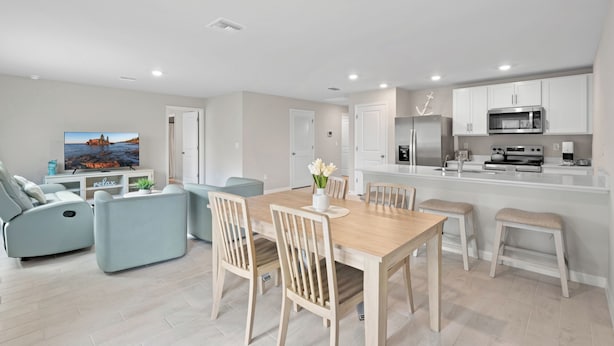 A modern living room with a flat-screen TV, a sofa, and a dining area with a wooden table and chairs. - Entire New House with Office Space-WiFi, Near JetBlue Park & RSW Airport! (Lehigh Acres)