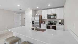 A modern kitchen with white cabinetry, stainless steel appliances, and a central island with a sink. - Entire New House with Office Space-WiFi, Near JetBlue Park & RSW Airport! (Lehigh Acres)