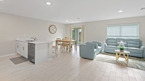 A modern kitchen with a built-in dishwasher, a dining area with a wooden table and chairs, and a living room with a light blue sofa and a coffee table. - Entire New House with Office Space-WiFi, Near JetBlue Park & RSW Airport! (Lehigh Acres)