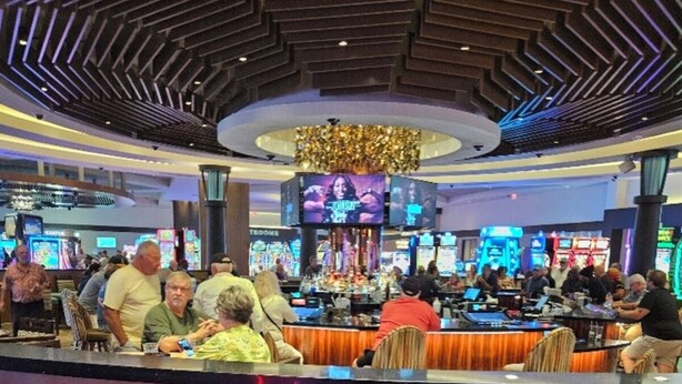 Un casino con una zona de bar central, máquinas tragamonedas y un gran candelabro.