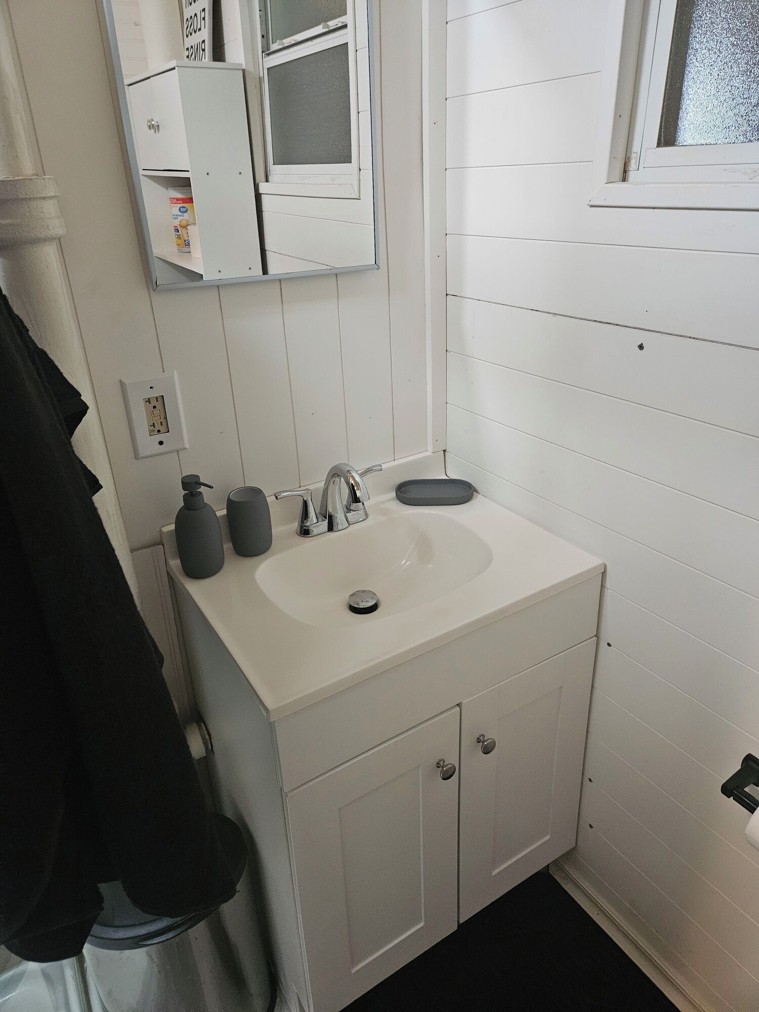 Une petite salle de bain blanche, avec un seul lavabo, un miroir et une fenêtre.