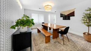 A modern dining area with a wooden table, black chairs, and a bench. There is a potted plant on a black console table and another plant in a basket on the floor. - Luxe & Spacious Retreat - Steps to Beach Game Room (Encinitas)