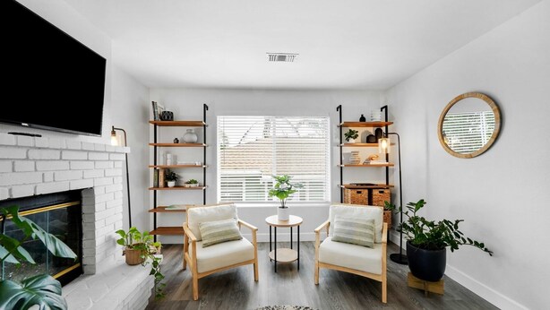 A living room with a white brick fireplace, two armchairs, a round coffee table, and built-in wooden shelving with plants. - Luxe & Spacious Retreat - Steps to Beach Game Room (Encinitas)
