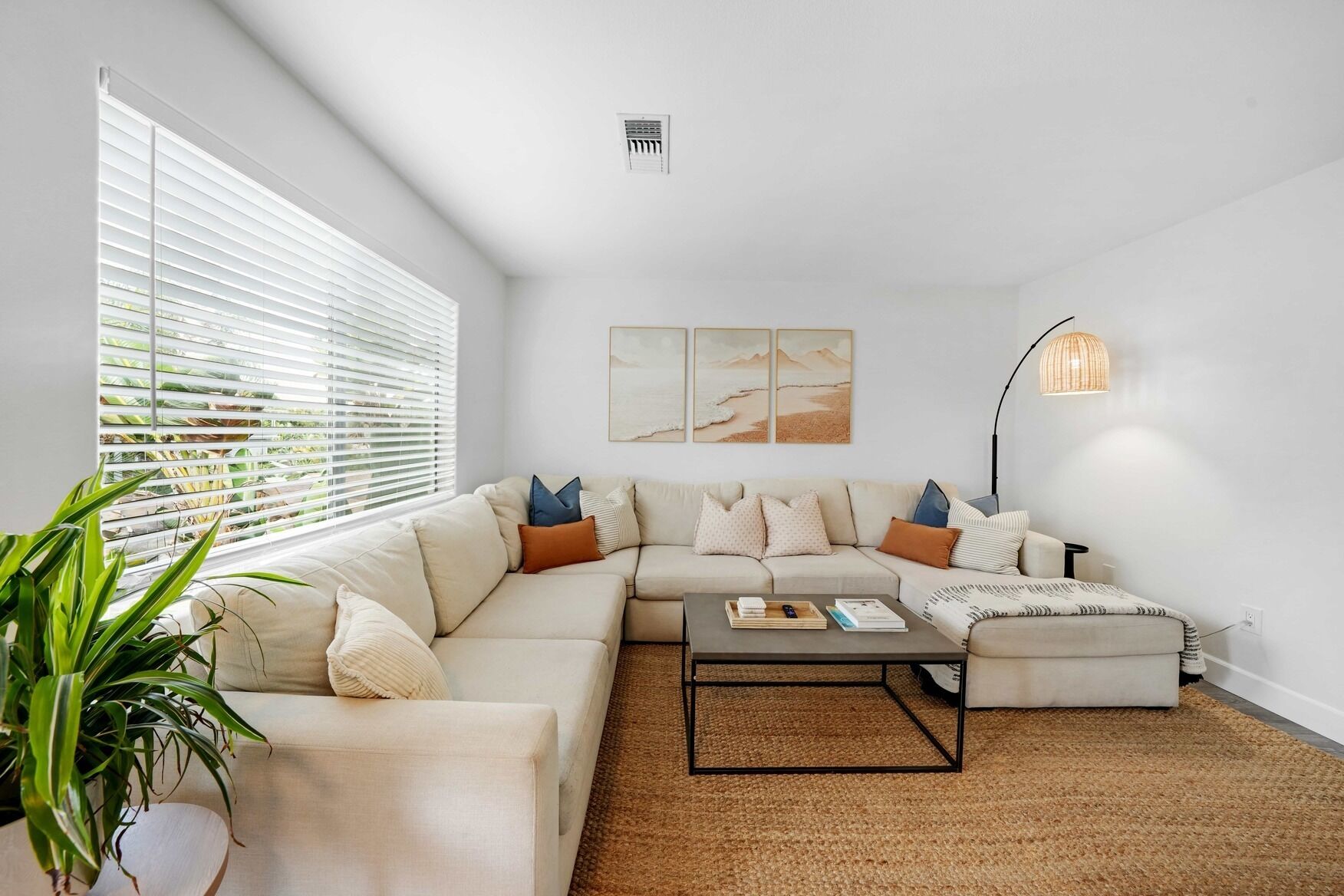 A modern living room with a sectional sofa, a coffee table, and a large window with blinds.