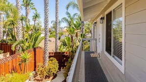 A covered porch with a wooden fence, palm trees, and a clear view of the backyard. - Luxe & Spacious Retreat - Steps to Beach Game Room (Encinitas)