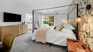 A modern bedroom with a bed, a TV, a desk, and a bathroom visible through an open door. - Luxe & Spacious Retreat - Steps to Beach Game Room (Encinitas)