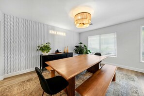 A modern dining room with a wooden table, black chairs, a black console, and a herringbone-patterned wallpaper. - Luxe & Spacious Retreat - Steps to Beach Game Room (Encinitas)