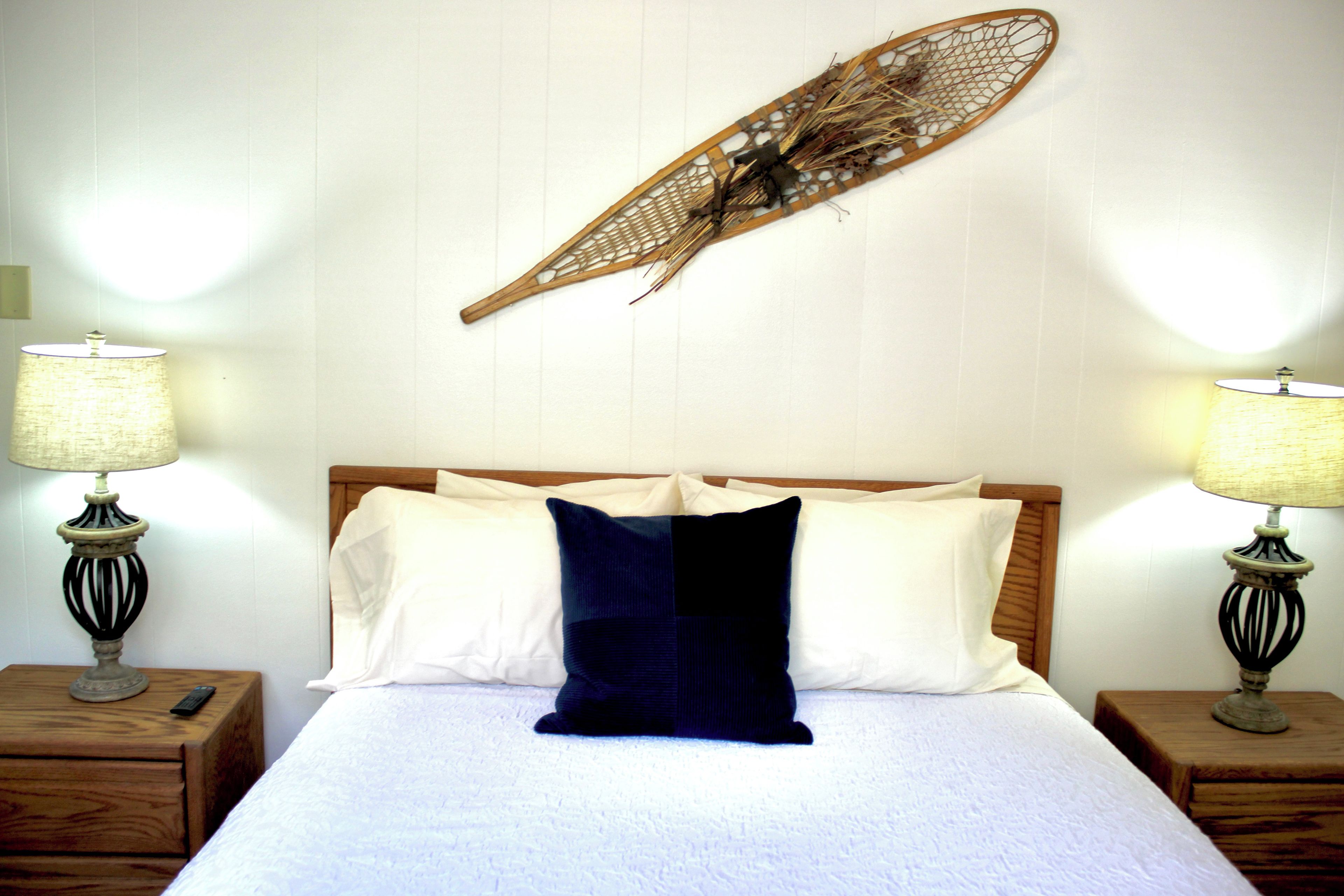 A neatly made bed with a wooden headboard, two bedside tables with lamps, and a wall-mounted decorative piece.