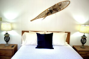 Ein ordentlich gemachtes Bett mit Holz-Kopfstück, zwei Nachttische mit Lampen und einem an der Wand befestigten dekorativen Element.