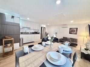 A modern kitchen with white cabinets, a stainless steel refrigerator, and a dining area with a round table set for four.