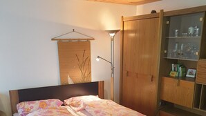 A double bed with floral bedding, a wooden wardrobe, a bedside lamp, and a small cabinet with glassware. - Landhaus Münz, quiet vacation apartment near Hopfen am See near Füssen (Hopferau)