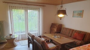A cozy room with a wooden dining table, a striped sofa, and a bed with a floral bedspread. - Landhaus Münz, quiet vacation apartment near Hopfen am See near Füssen (Hopferau)