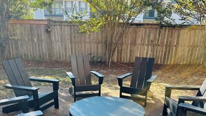 Un jardin avec une clôture en bois, une table ronde et six chaises Adirondack.