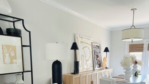 Un salon avec un canapé en osier, un fauteuil blanc et un meuble en bois orné d’œuvres d’art.