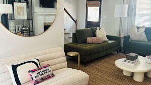 Un salon avec un grand miroir rond, un canapé vert, un canapé blanc et une table basse.
