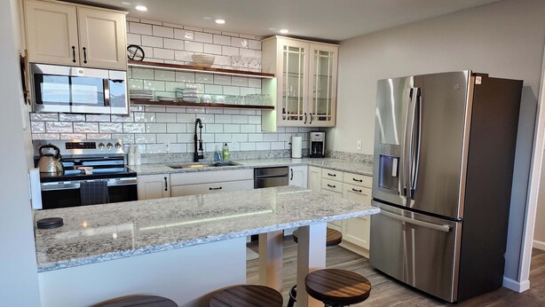 A modern kitchen with a stainless steel refrigerator, granite countertops, and white cabinetry. - Escape to Spicer and enjoy stunning lake views from this comfortable 2-bedroom! (Spicer)