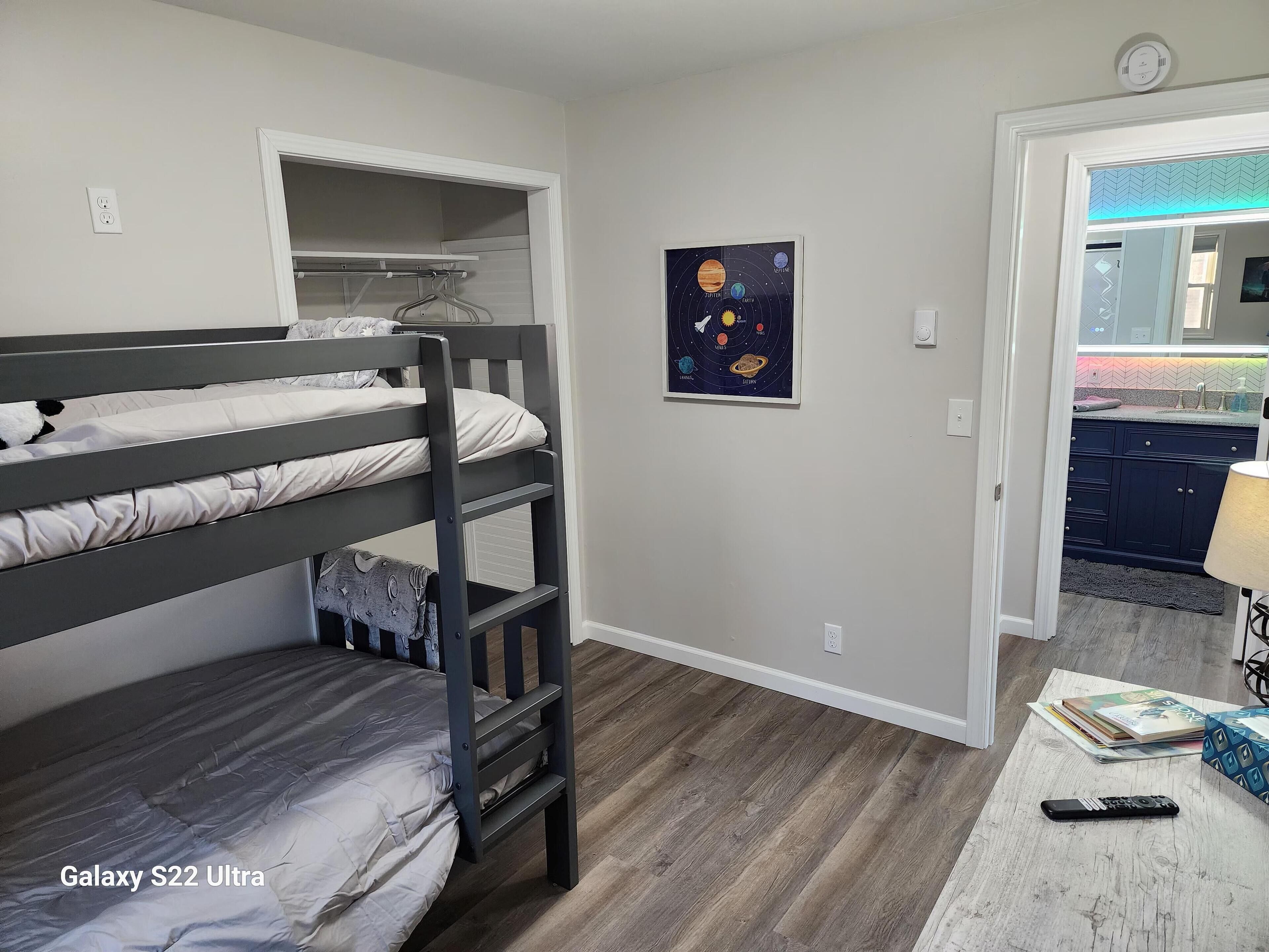 A bedroom with a bunk bed, a wall-mounted shelf, a galaxy-themed wall art, and a view into the kitchen.