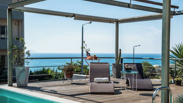 Un espace aménagé au bord de la piscine, avec des chaises longues et des plantes en pot, offrant une vue dégagée sur la mer.