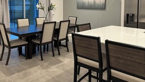 A modern dining area with a large table and chairs, a water dispenser, and a kitchen area with a refrigerator. - Grand Resort Home in Resort with Pool (Kissimmee)