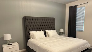 A neatly made bed with a tufted headboard, white bedding, and two bedside tables with lamps. - Grand Resort Home in Resort with Pool (Kissimmee)