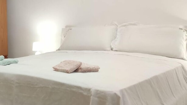 Een slaapkamer met een bed, kussens en een nachtkastje.