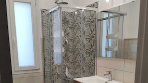 Een badkamer met een douchecabine van glas, een toilet, een wastafel en een wasmachine.