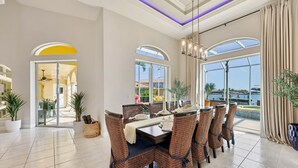 A dining area with a table set for six, surrounded by wicker chairs, large windows offering a view of the sea, and a ceiling with purple lighting. - Sunset view villa (Cape Coral)