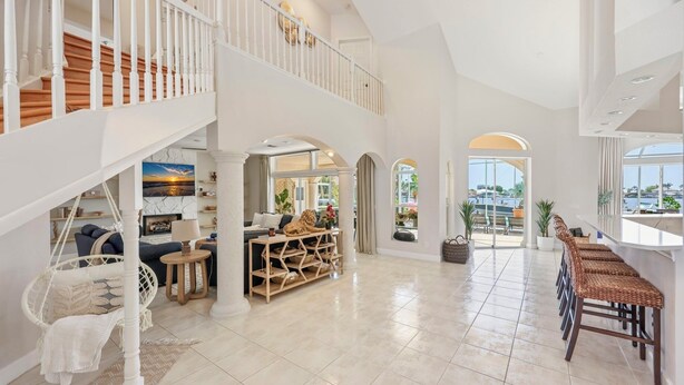 A spacious interior with a high ceiling, a staircase, a seating area with a sofa and a hanging chair, and a bar area with wicker chairs. - Sunset view villa (Cape Coral)