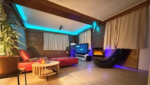 A cozy living room with a sofa, a coffee table, a TV, and a fireplace. - House Bernstein, Apartman 3 (Haus im Ennstal)