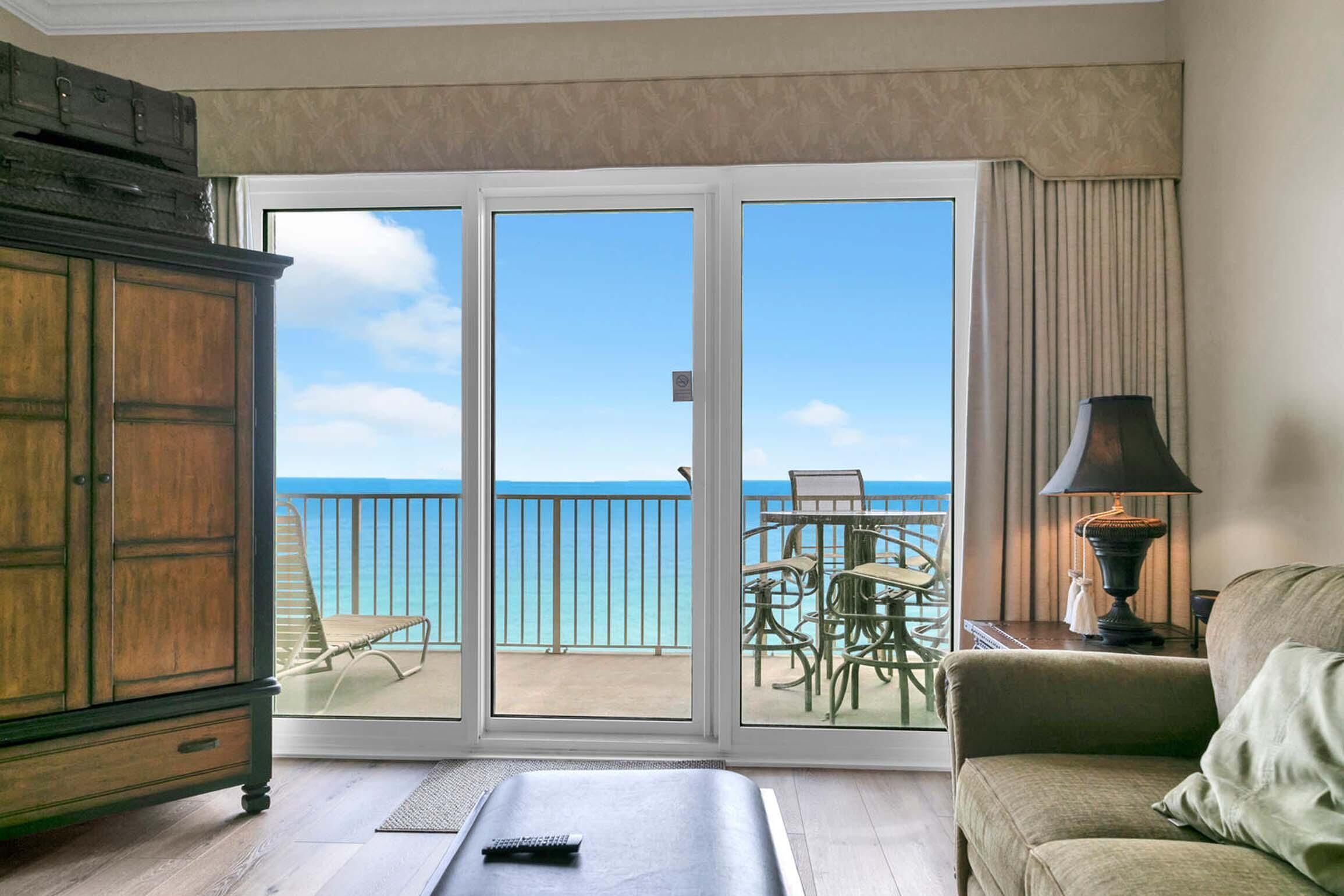 A room with a view of the ocean, a sliding glass door, a wooden cabinet, a sofa, and a table with a lamp.