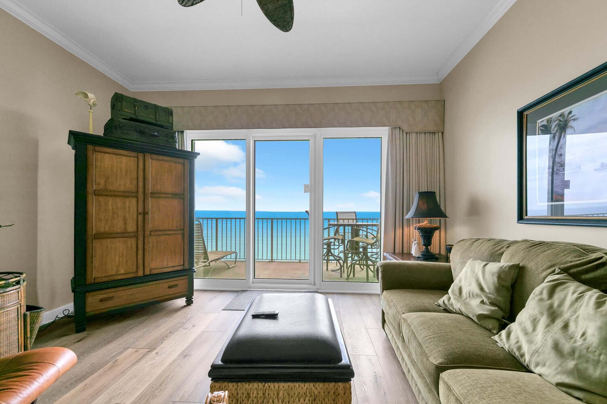 A living room with a sofa, a cabinet, and a view of the ocean through large glass doors.