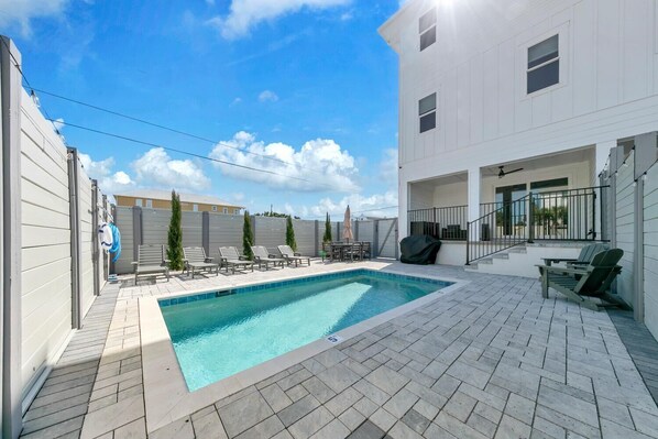 A swimming pool with lounge chairs and a covered seating area, surrounded by a white building with a covered patio. - Golden Seashell East (Panama City Beach)