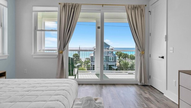 A bedroom with a large sliding glass door leading to a balcony, a bed, and a dresser. - Golden Seashell East (Panama City Beach)