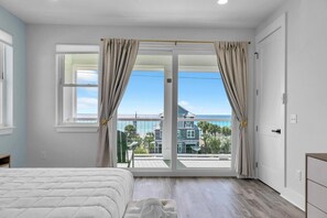A bedroom with a large sliding glass door leading to a balcony, a bed, and a dresser. - Golden Seashell East (Panama City Beach)