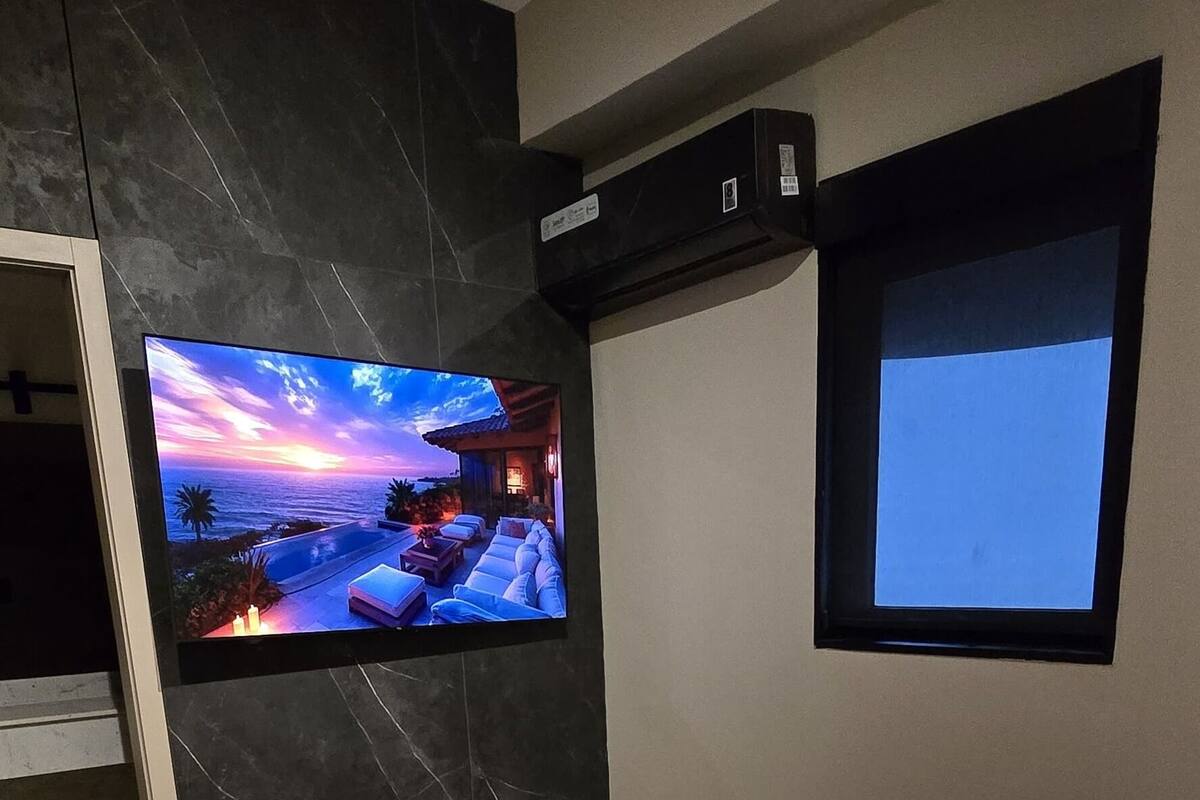 A bedroom with a large bed, a TV mounted on the wall, and a small window.