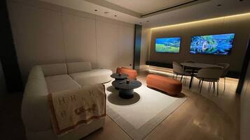 Una sala moderna con un sofá, un reposapiés, una mesa de centro y un televisor montado en la pared.