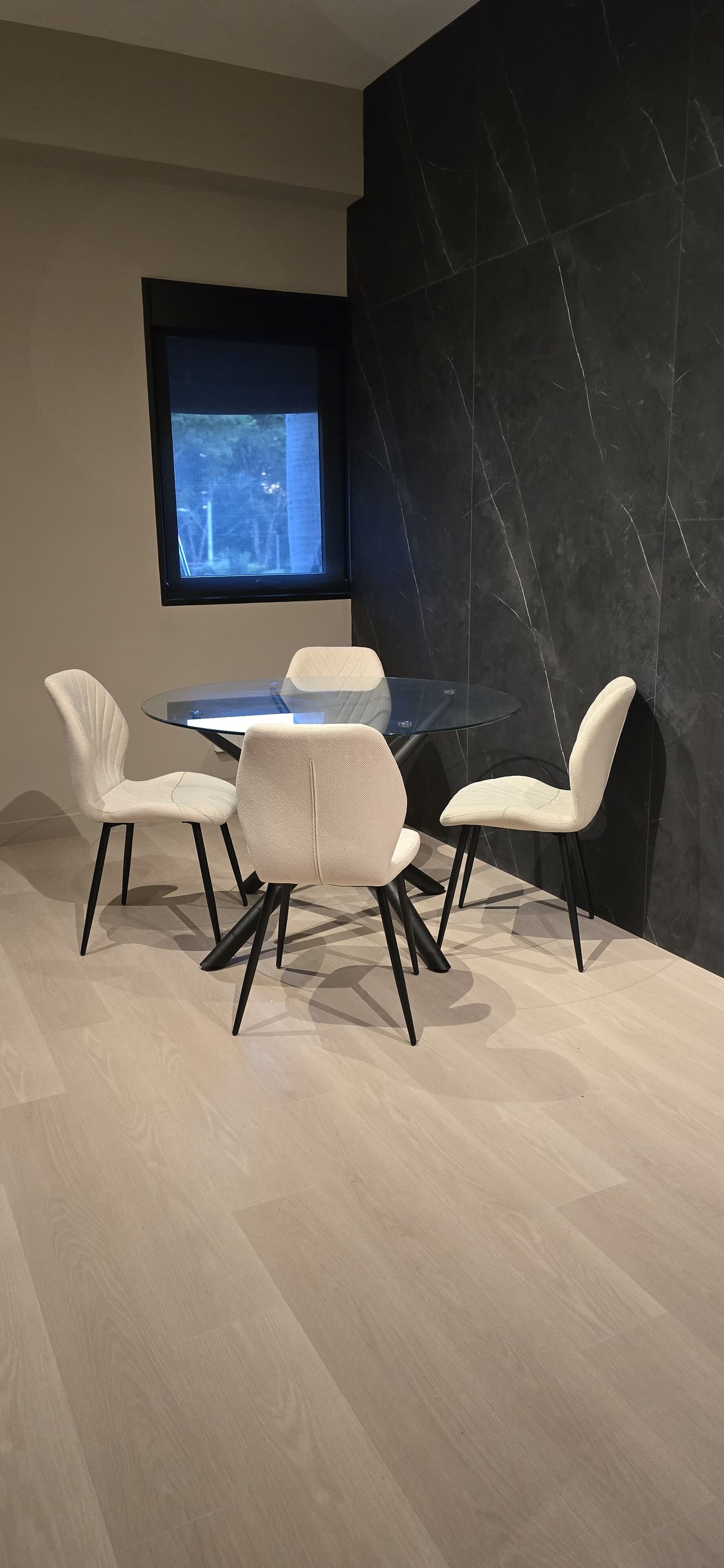 Un comedor moderno con una mesa de vidrio y cuatro sillas blancas con patas negras.