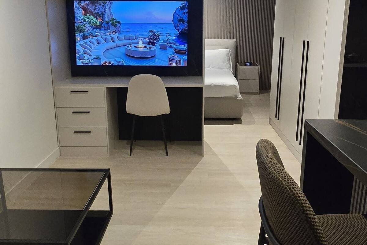 A modern living room with a flat-screen TV, a sofa, a coffee table, and a dining area.