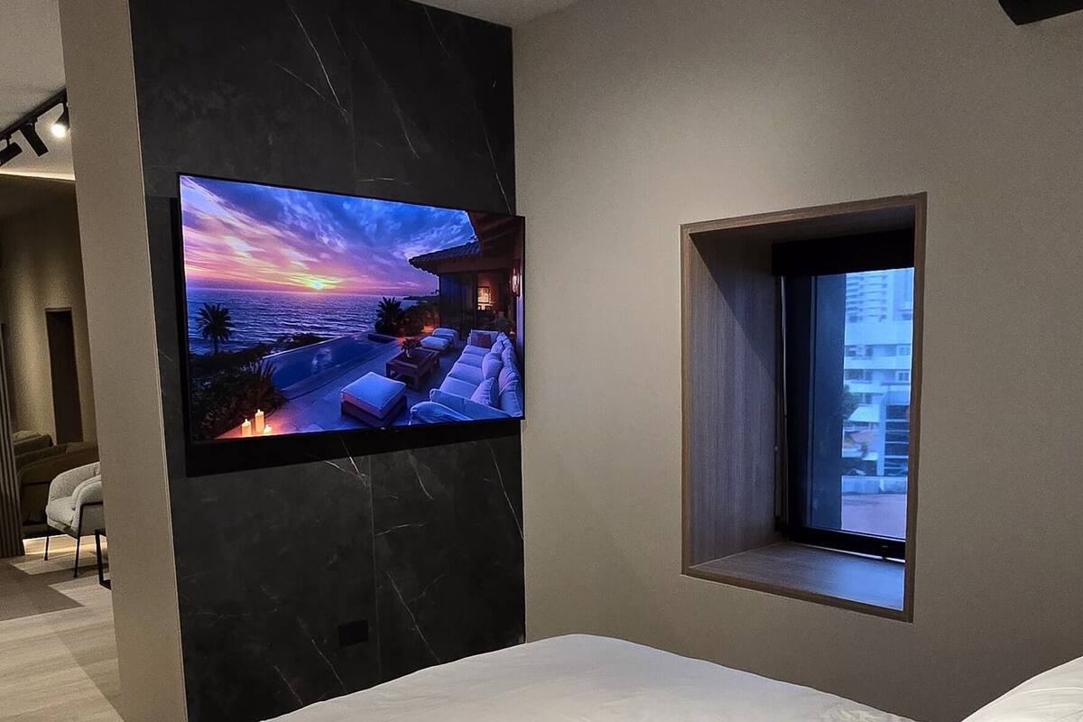 A modern bedroom with a large bed, a mounted TV, and a small window.
