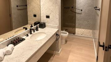 A modern bathroom with a marble vanity, a large mirror, a shower with glass doors, and a toilet.