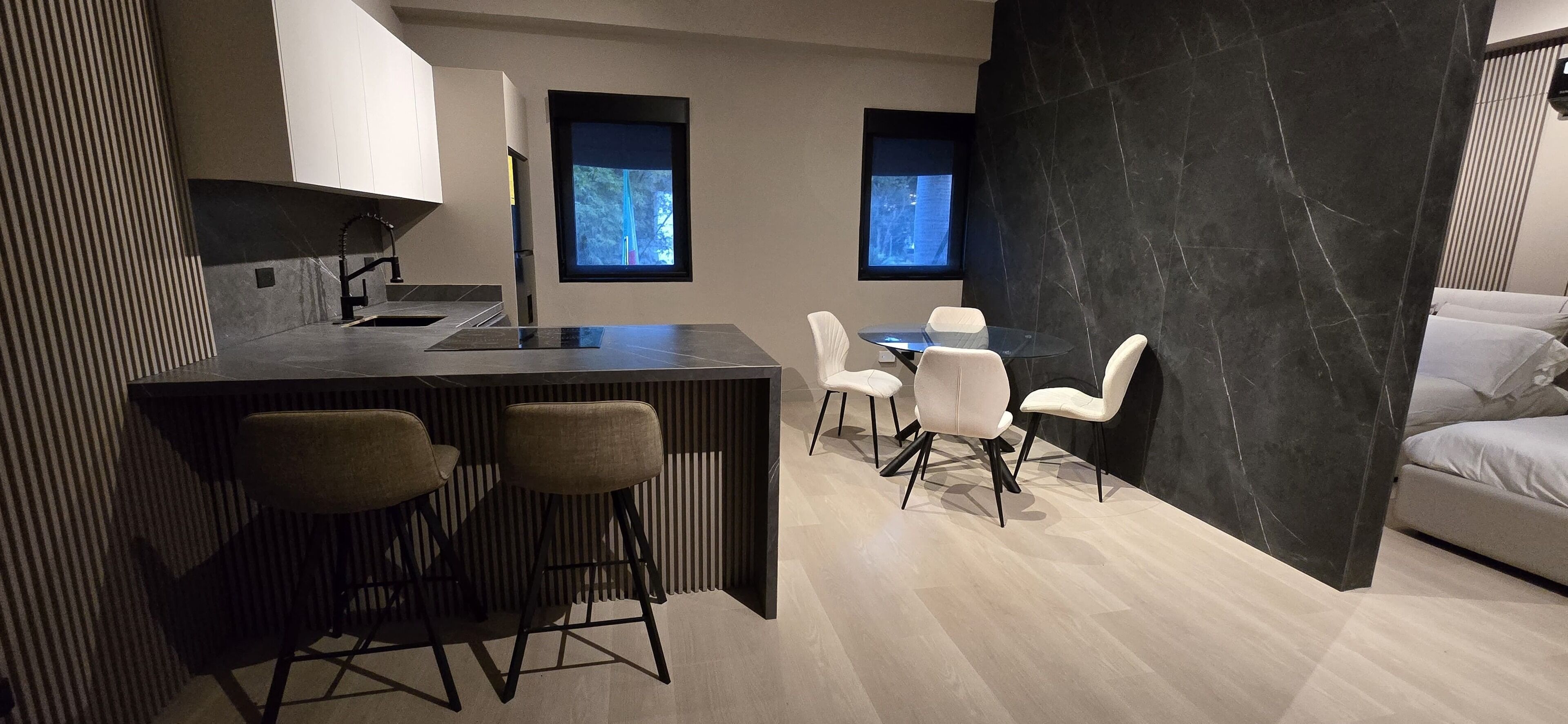 A modern kitchen with a bar area, two windows, and a dining area with white chairs.